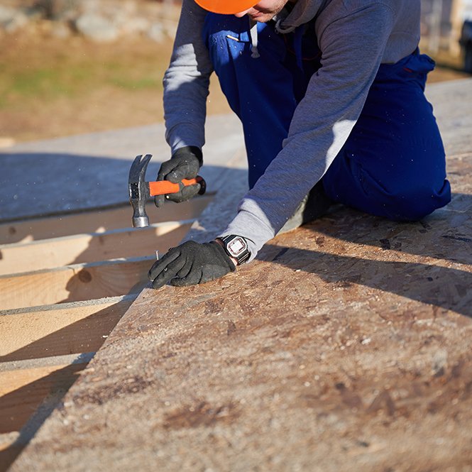 Carpenter hammering nail into OSB panel while building wooden frame house.